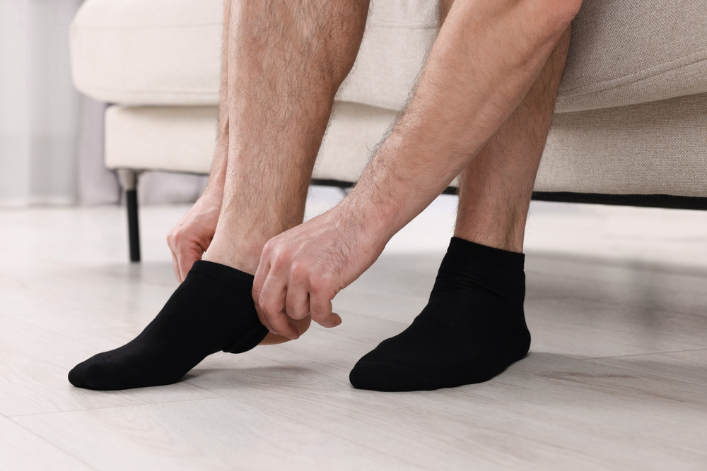 Man putting on black socks at home, closeup